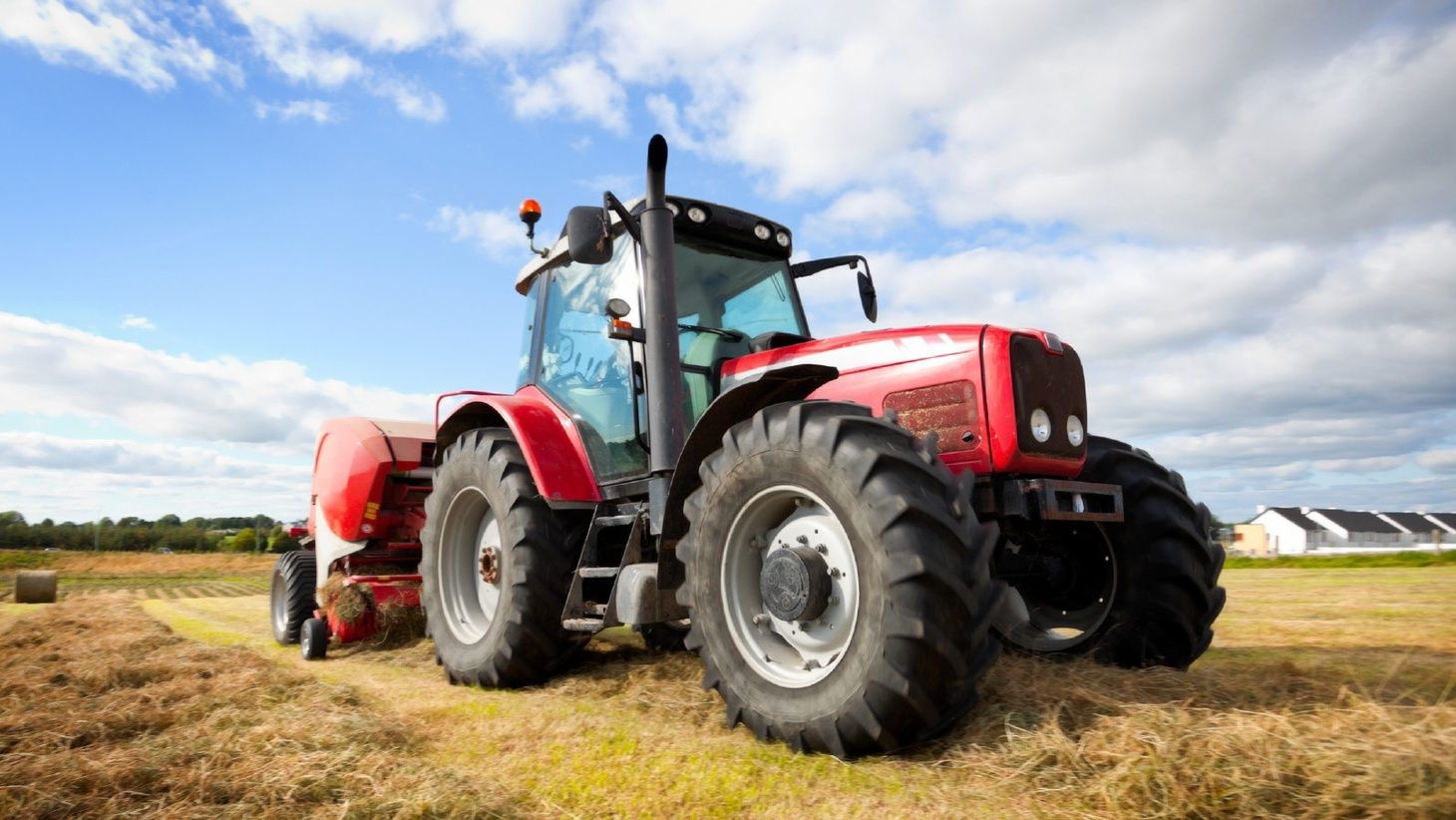 Ein Traktor sammelt Heu auf einer gemähten Wiese